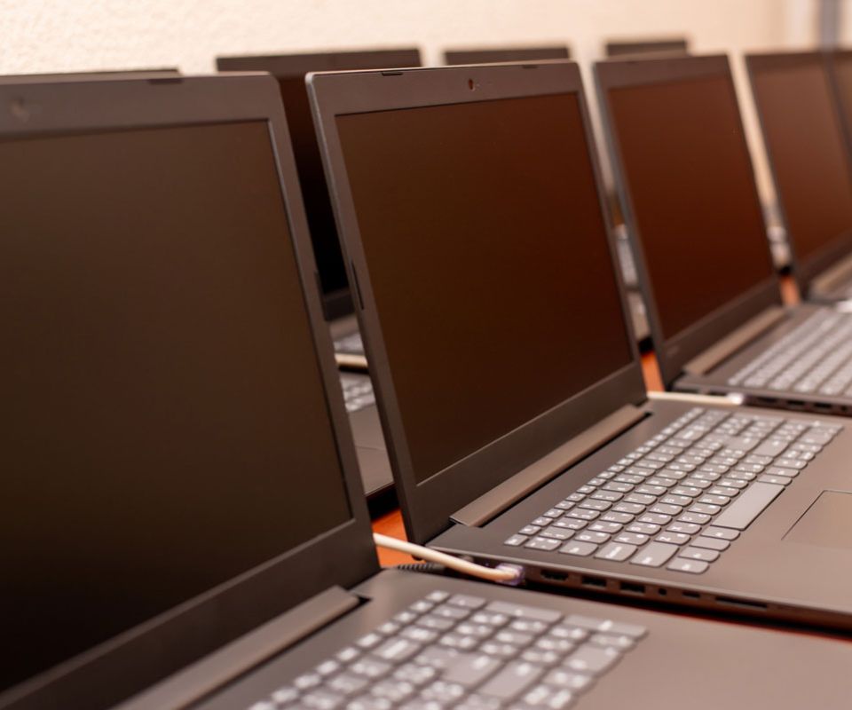 A row of black laptops neatly arranged on a table, showcasing their sleek design and uniform appearance.