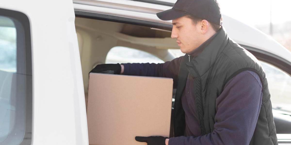 Delivery worker unloading a sealed cardboard box from the back of a white service van.