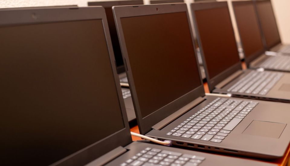 A row of black laptops neatly arranged on a table, showcasing their sleek design and uniform appearance.