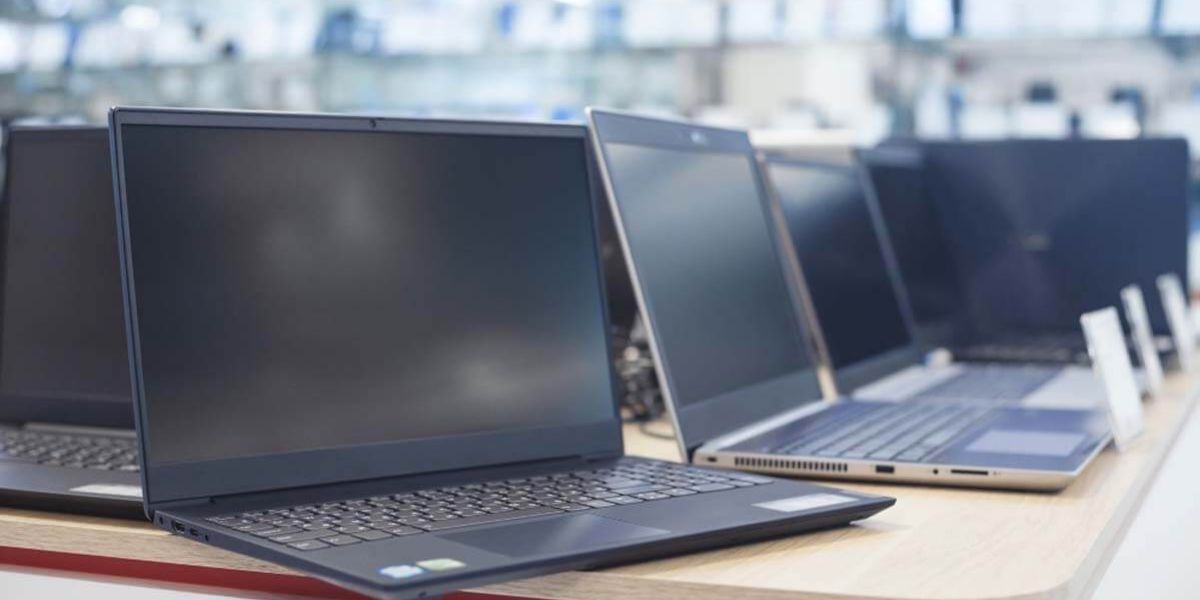 Rows of laptop computers displayed on a retail showroom counter, with additional devices visible in the background.