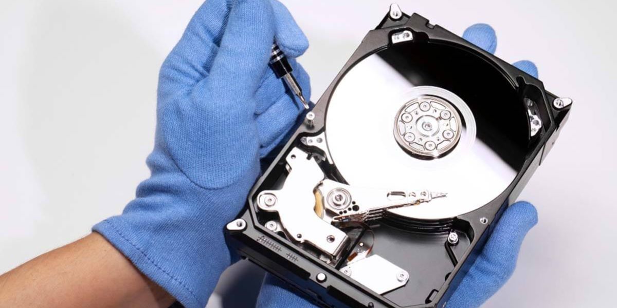 Technician wearing protective gloves disassembling an open hard disk drive with a precision screwdriver